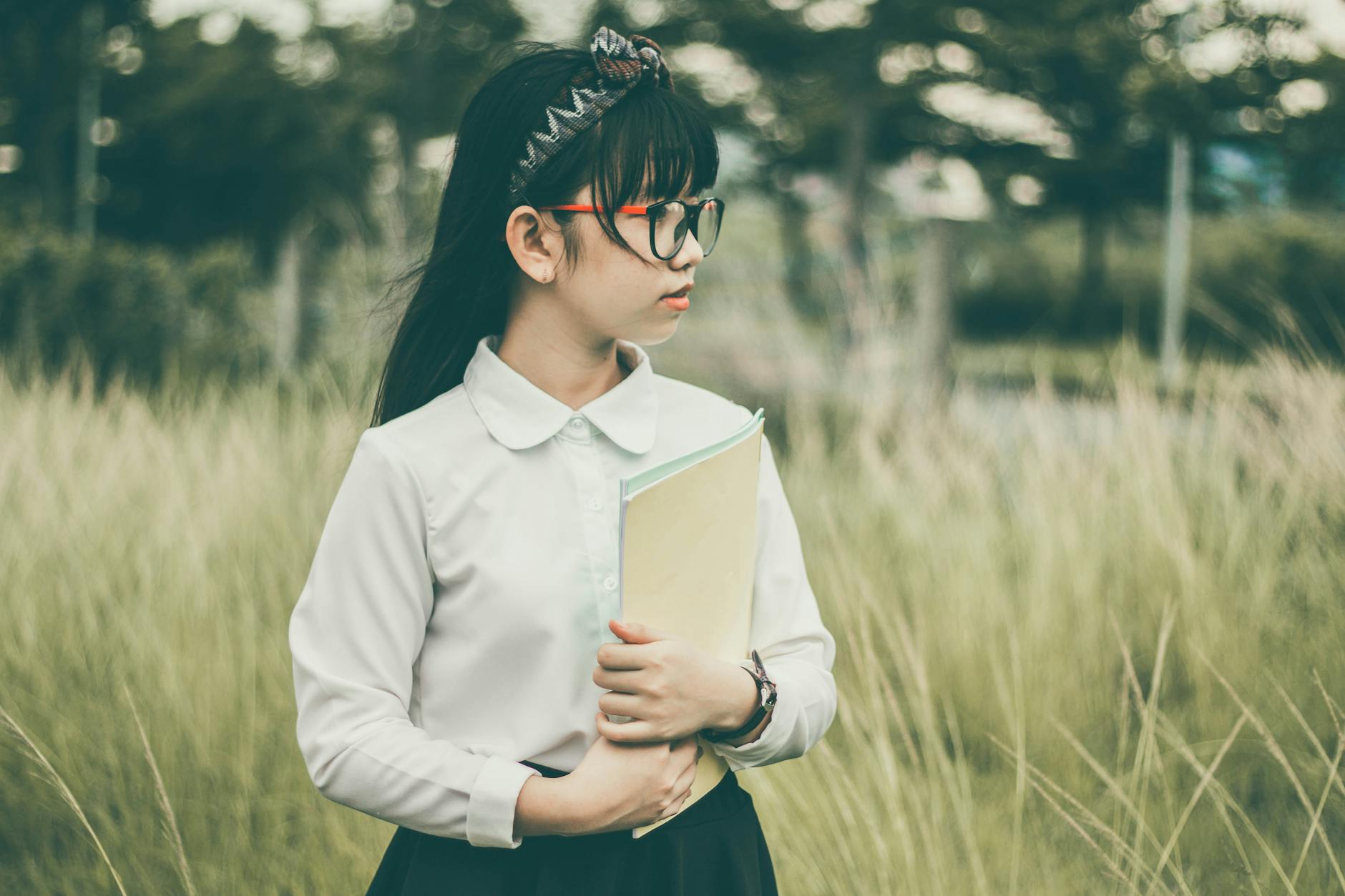 girl in white long sleeved shirt and black bottoms holding brown folder