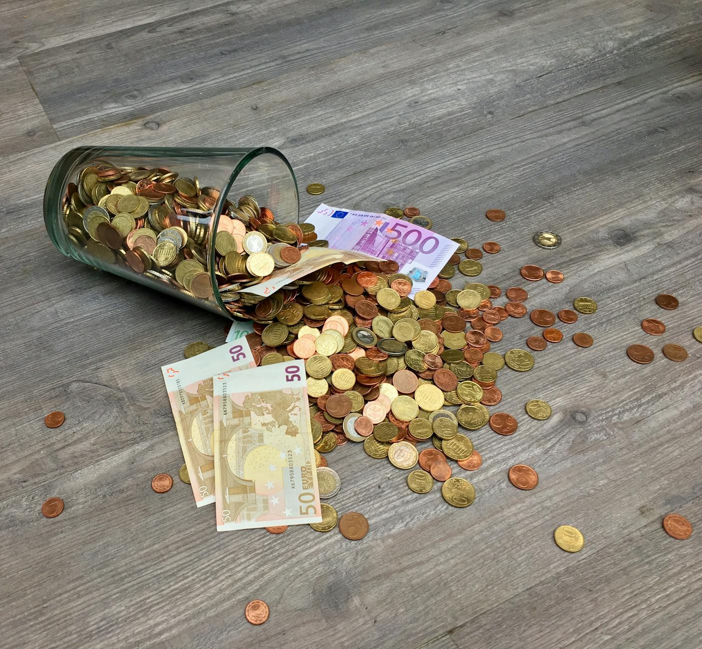 coins and banknotes scattered on gray wooden surface