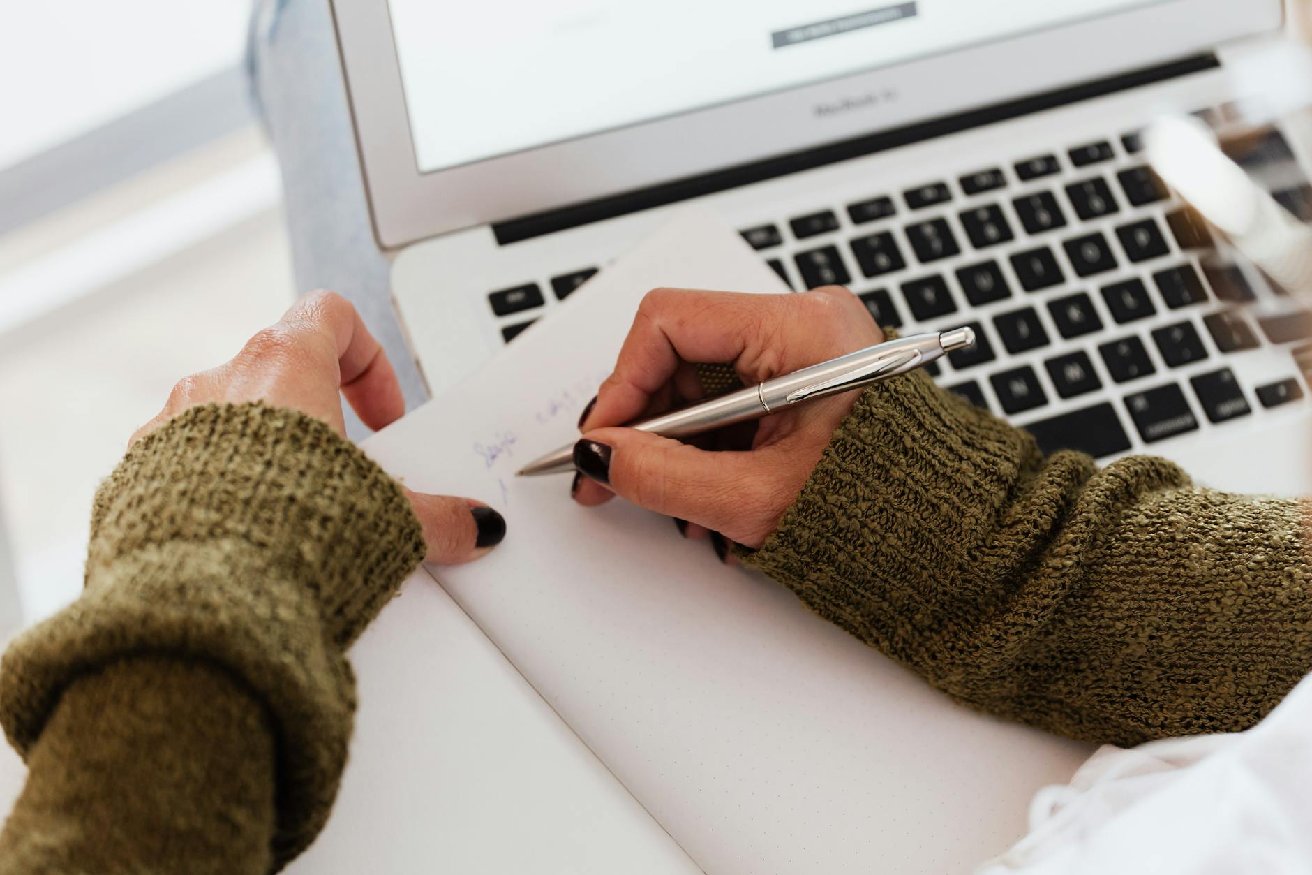 crop woman taking notes while working on laptop