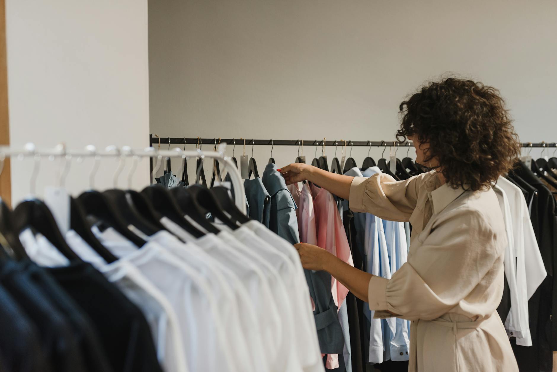 woman in beige long sleeves choosing clothes from the clothes rack