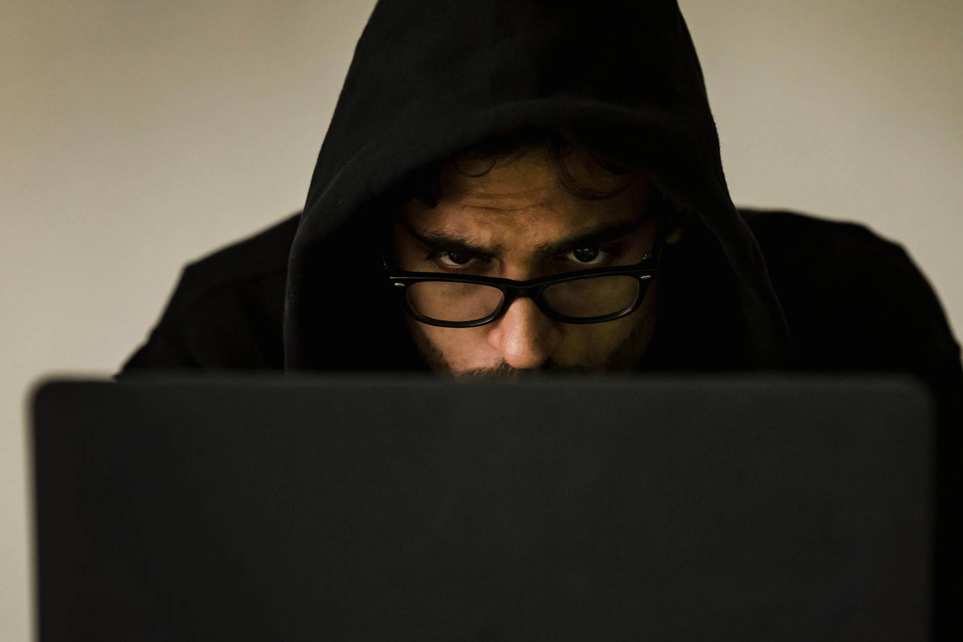 crop focused hacker in hood using laptop