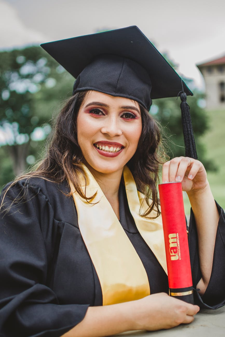 selective focus portrait photo of smiling woman in black academic dress holding diploma posing