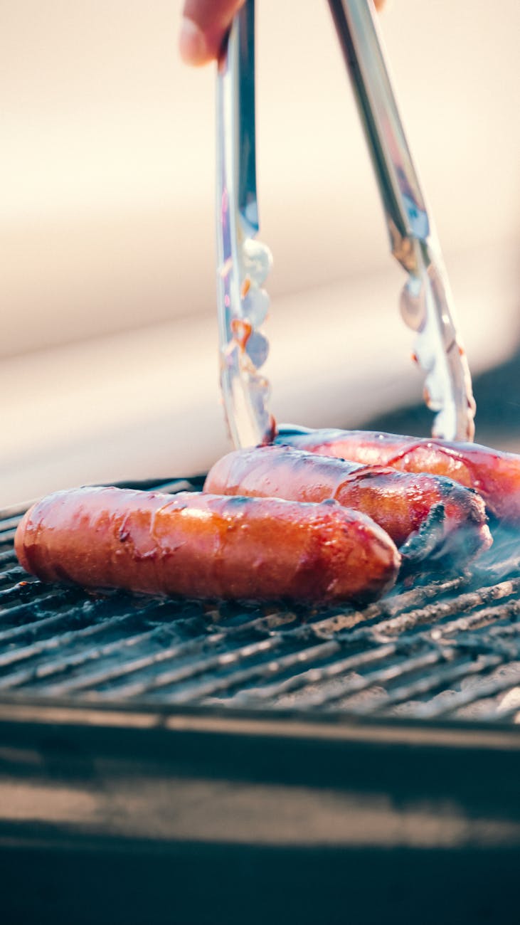 grilled sausages on bbq grill with tongs
