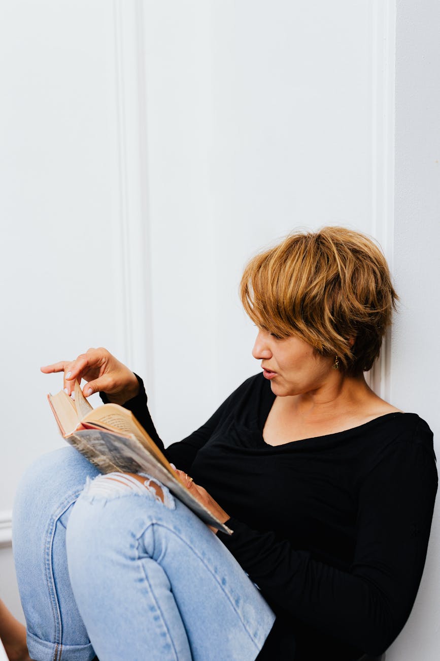 woman in black shirt and blue denim jeans sitting reading a book