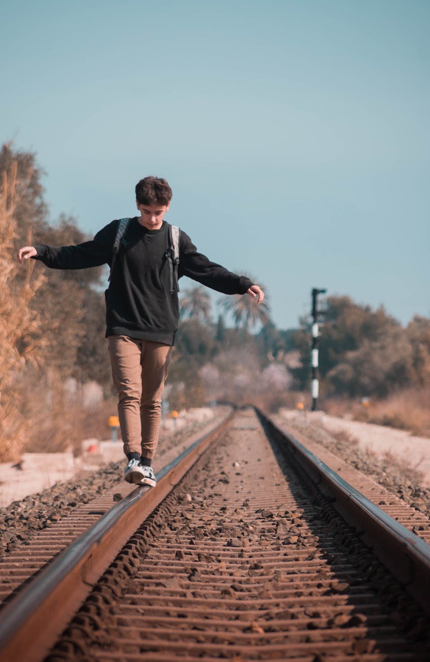 man in black sweater walking on train rail