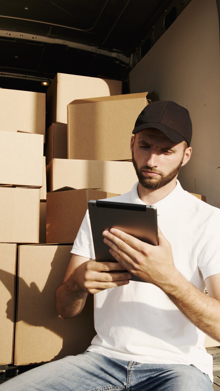a man in white shirt holding an ipad while sitting near the boxes