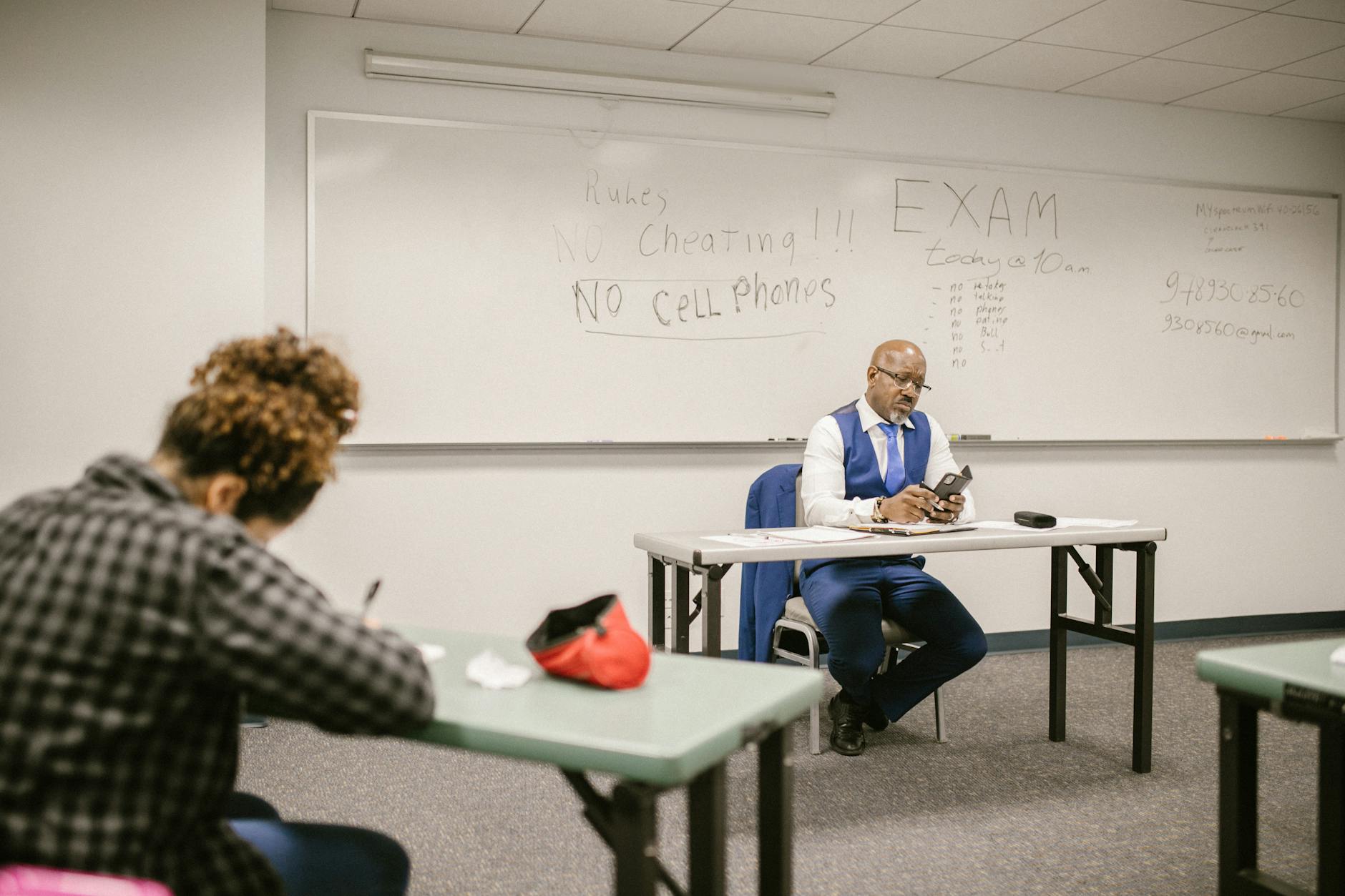 teacher using his smartphone while proctoring his students during an exam