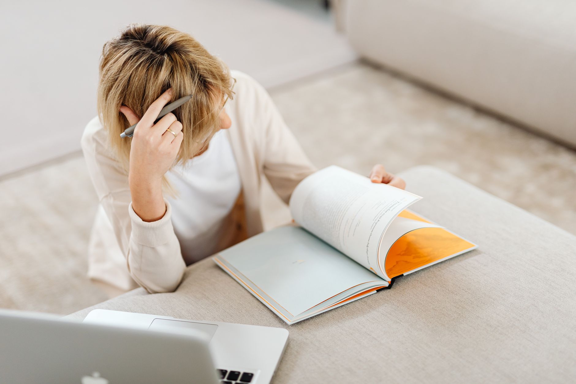 woman reading book with laptop and pen in hand