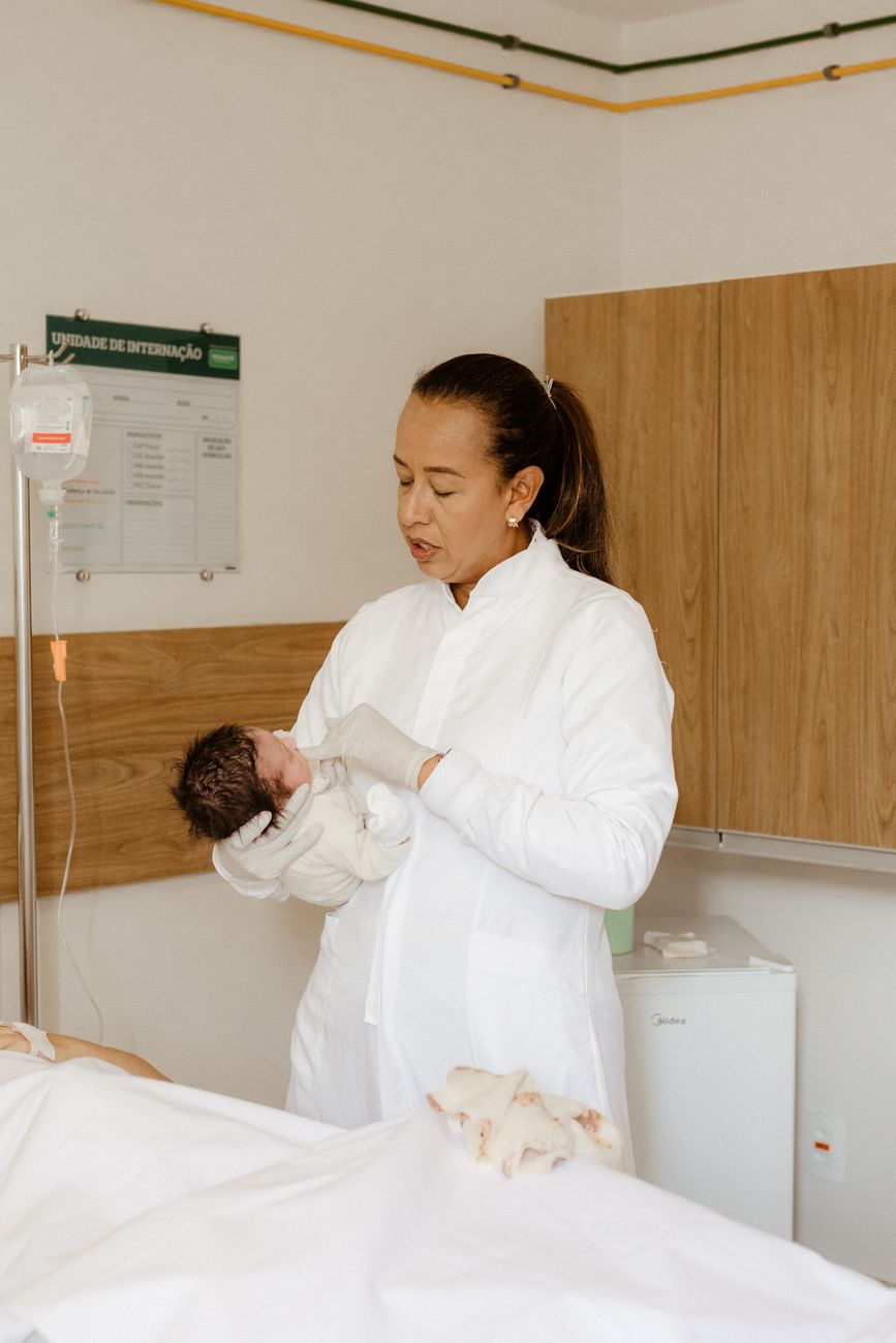 a woman in white coat holding a baby in a hospital bed