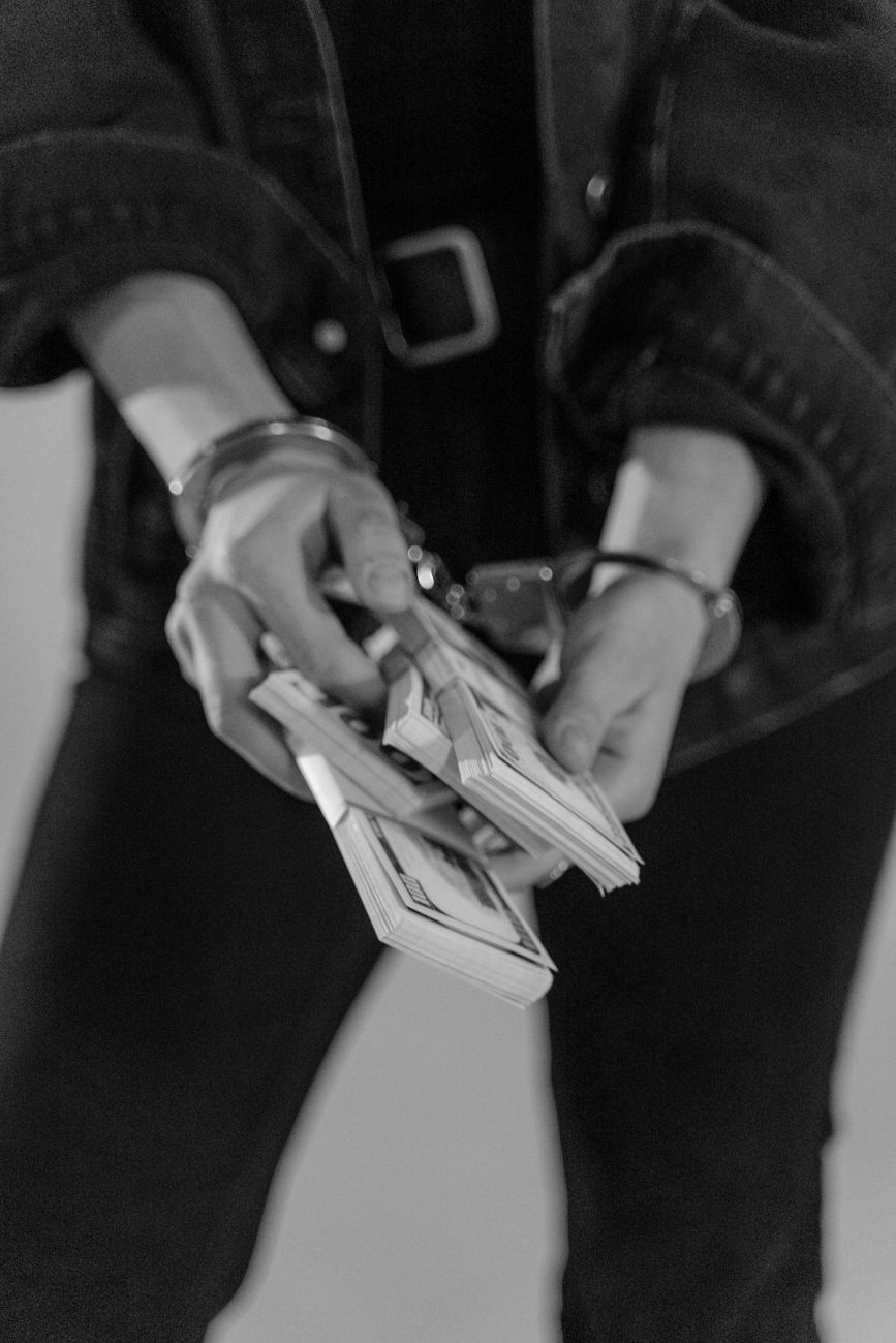grayscale photo of handcuffed person holding bundles of cash money