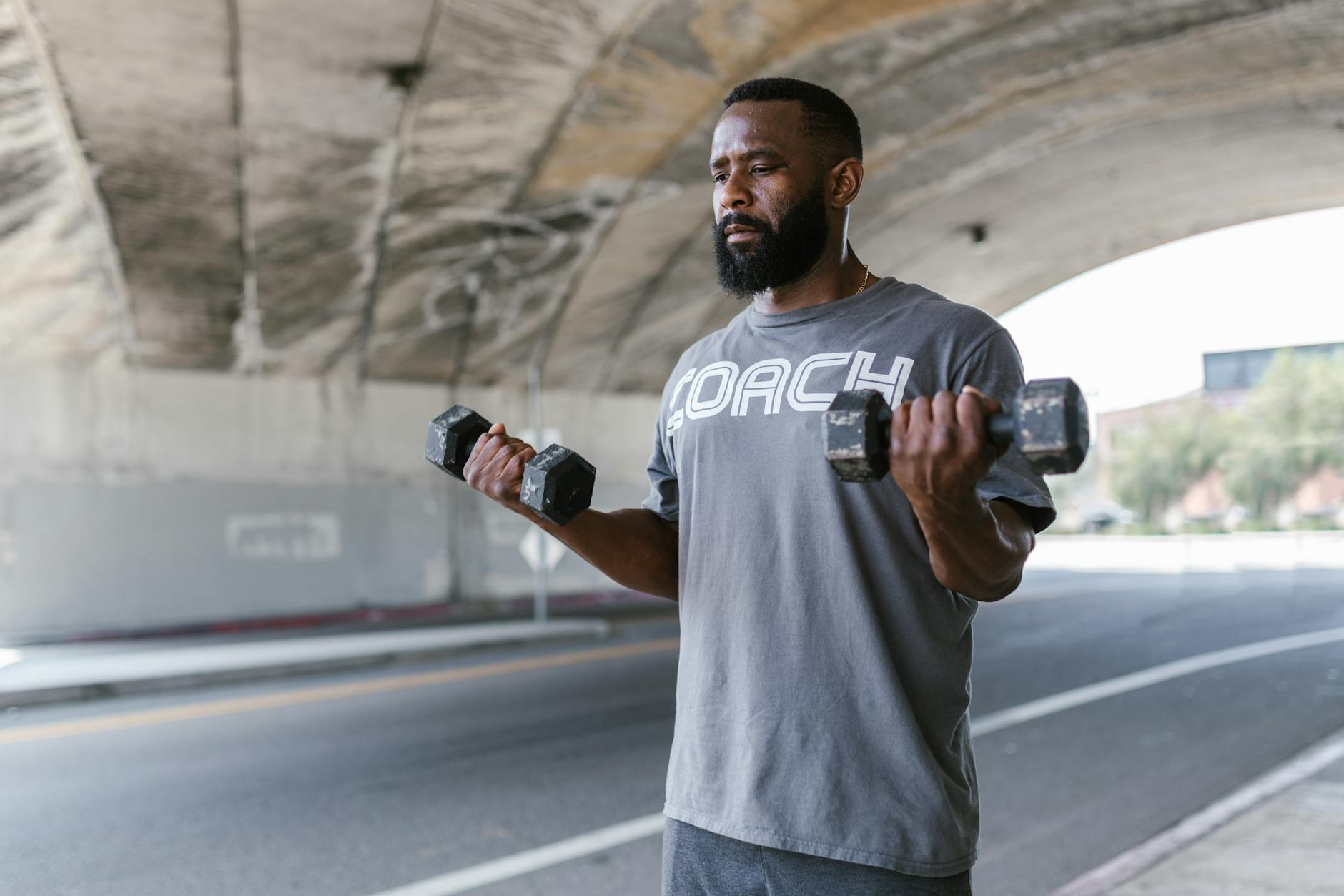 bearded man holding weights on both hands on side walk