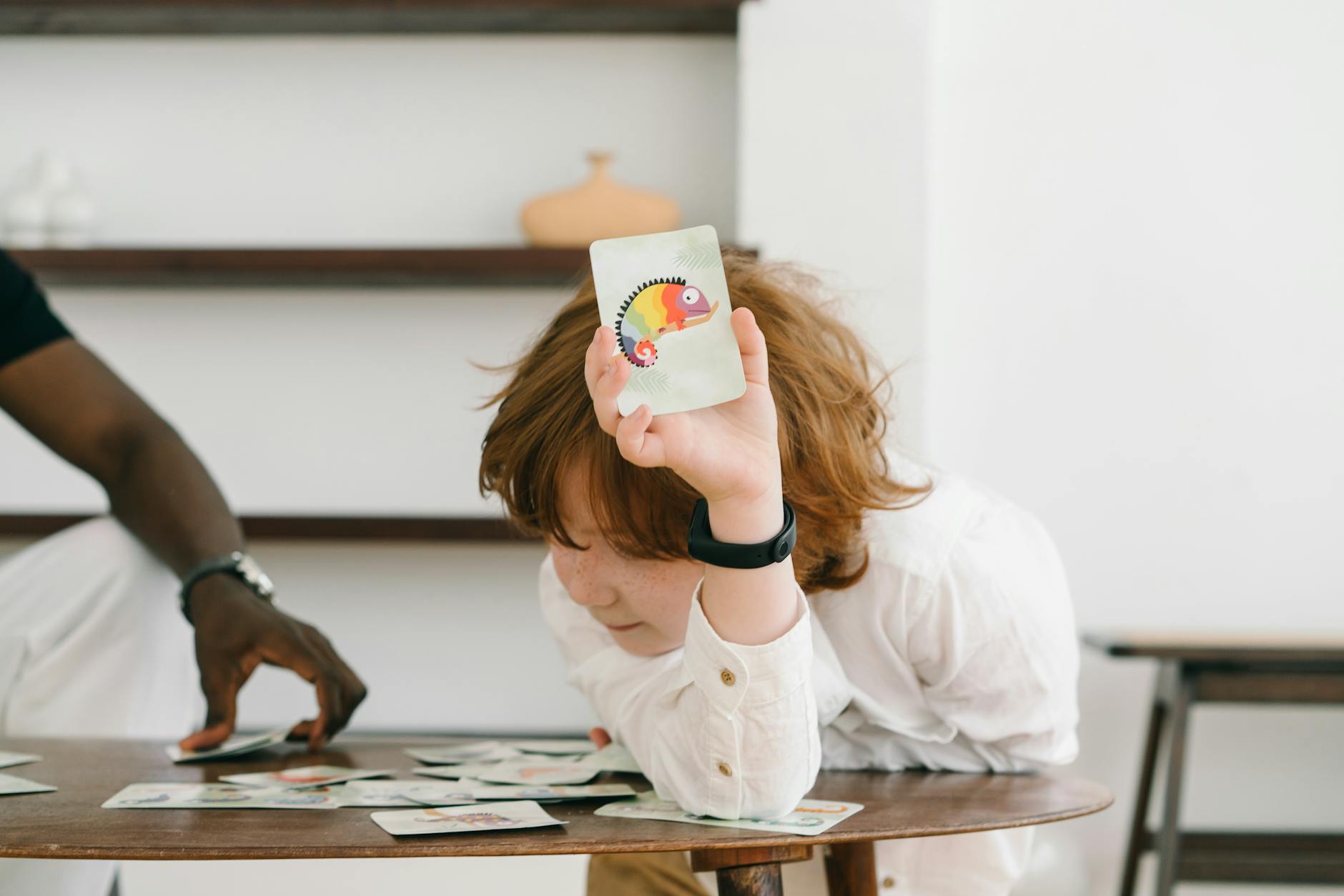 a child in white polo holding up a chameleon flash card