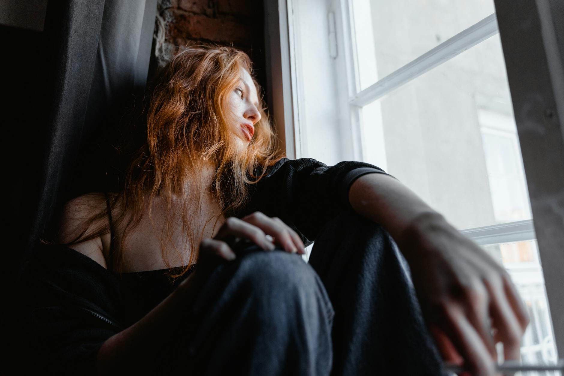 woman sitting on window sill looking outside